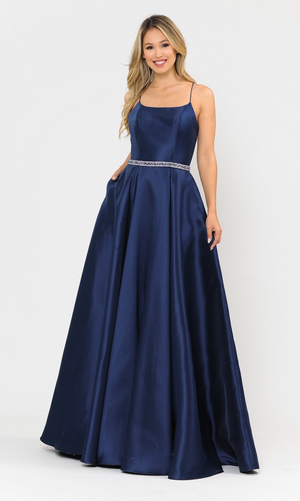 A woman in the Scoop-Neck Long A-Line Prom Dress with Pockets 8684, a sleeveless, floor-length navy gown with a fitted bodice and thin straps, stands against a plain white background.